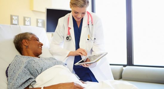 Doctor With Digital Tablet Talks To Woman In Hospital Bed